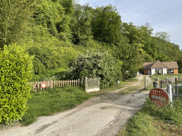 Le chemin qui monte en forêt commence ici à gauche, avec un passage pour piétons entre les deux barrières de bois.