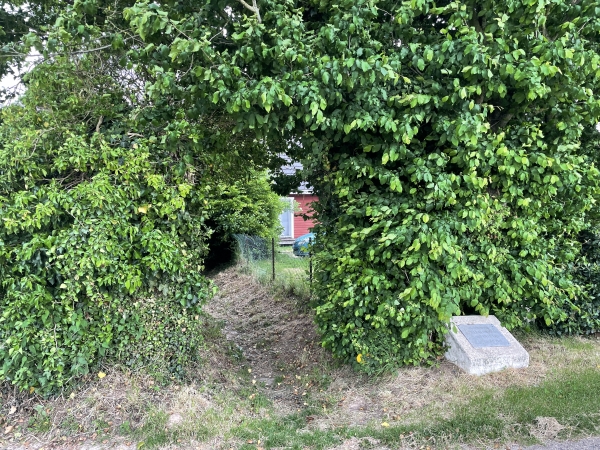 Nous traversons le Thuit-Simer par ce discret chemin. A remarquer, à droite, la stèle anonyme en mémoire d'un soldat américain, tombé en ce lieu le 22 août 1944.